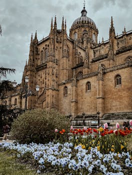 Beautiful view of a historic Gothic cathedral in Salamanca with a vibrant spring flower garden.