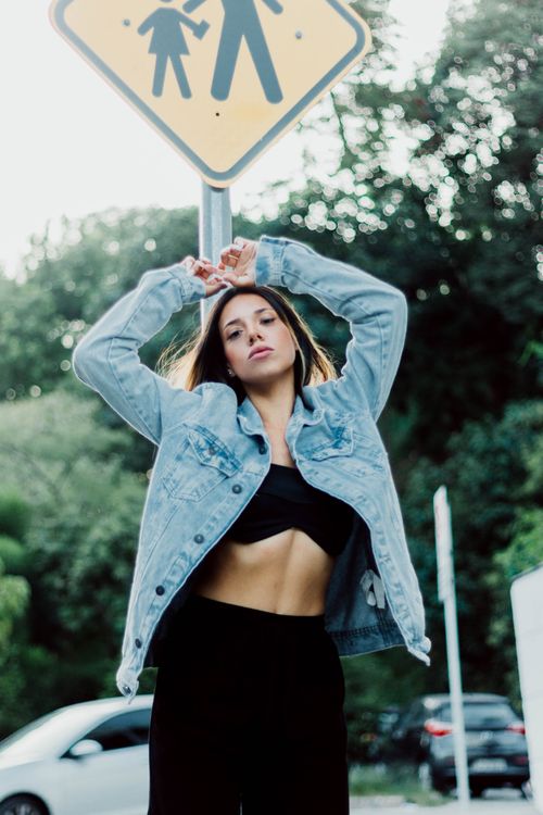 Free Casual portrait of a young woman in a denim jacket posing outside beneath a road sign. Stock Photo