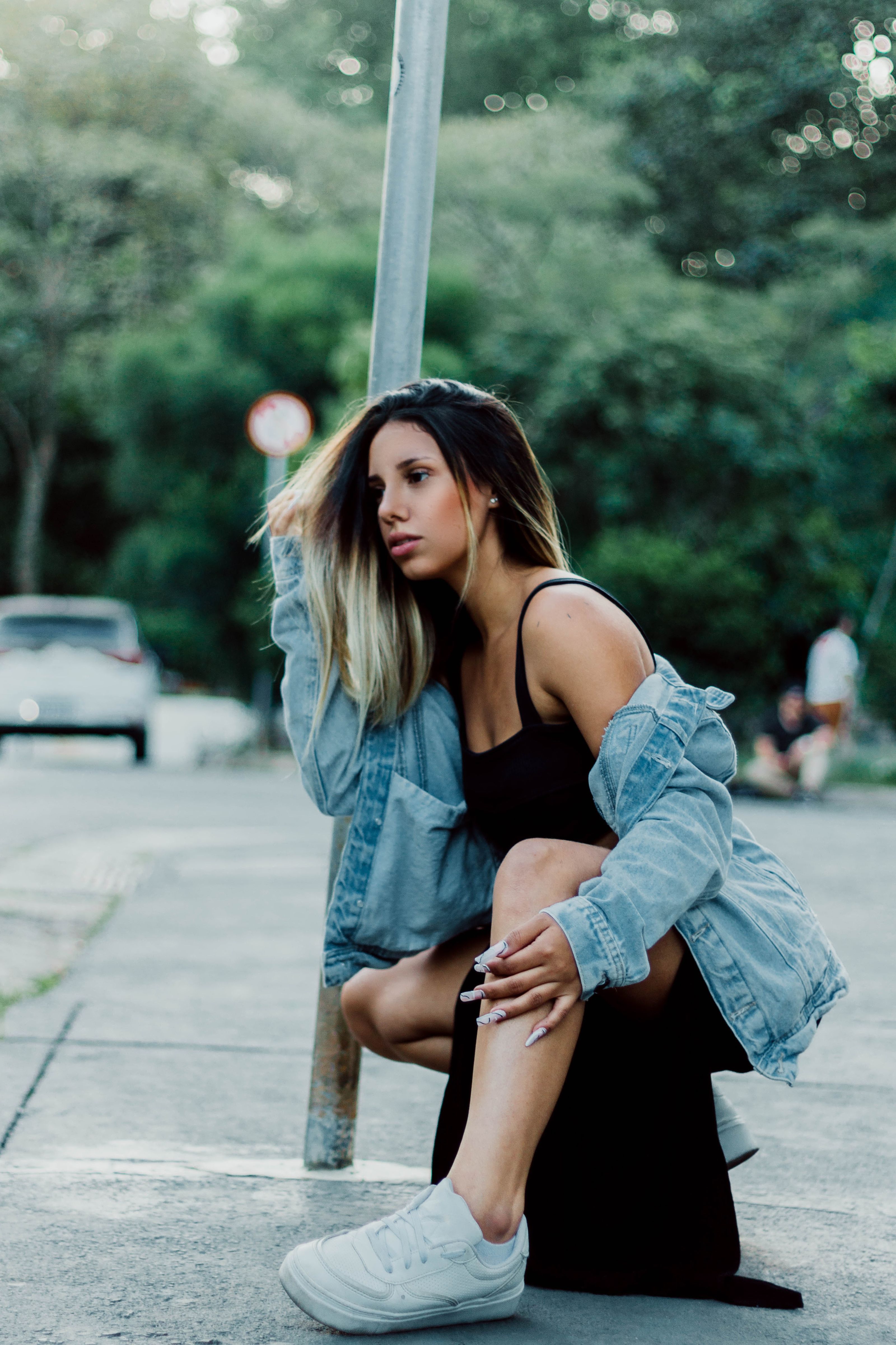 Mulher com jaqueta de denim e vestido preto posando ao ar livre, exibindo moda de rua.