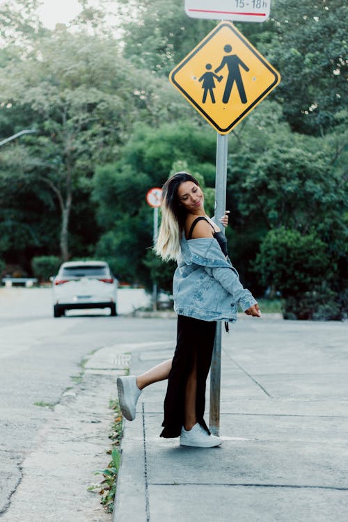 Woman in Denim Jacket Standing on Road Sign