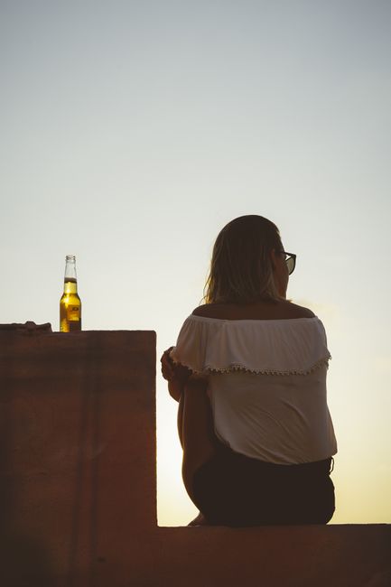 A woman sitting on a ledge with a beverage at sunset in Tel Aviv.