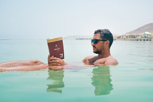 Homem Usando óculos De Sol, Lendo Um Livro Sobre Um Corpo D'água