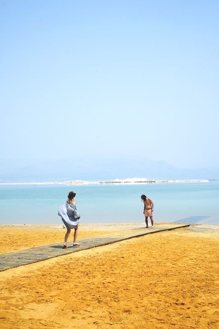 Two people enjoy a sandy beach with a clear blue sea under a sunny sky, perfect for a leisure day.