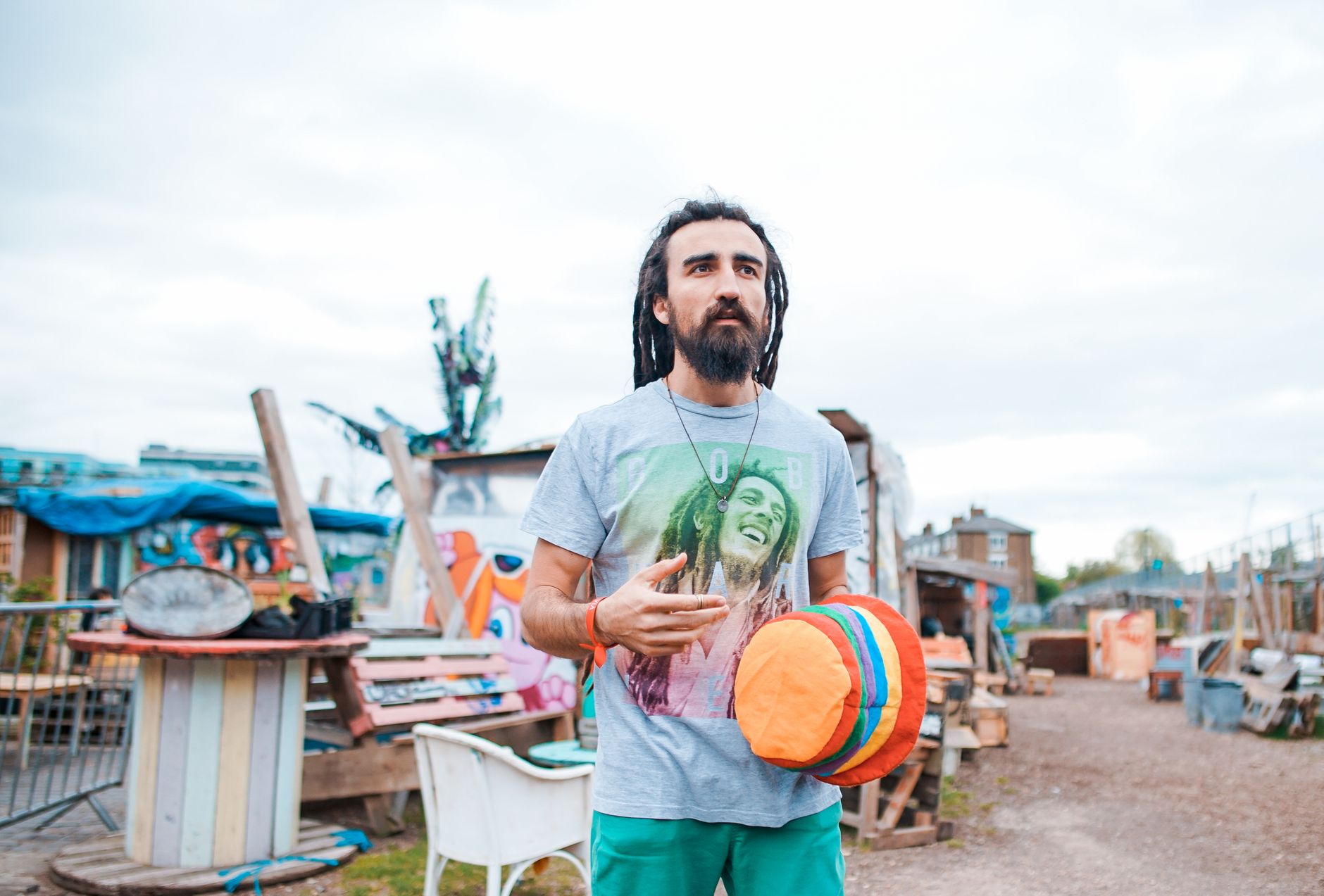Man with dreadlocks holding a colorful hat in an outdoor creative space in London.