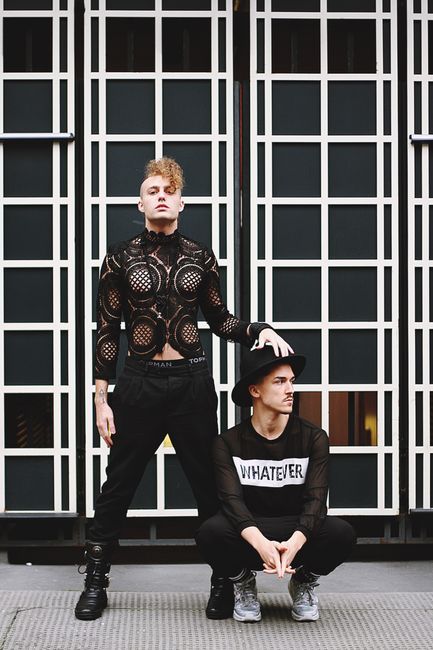 Two men in contemporary fashion poses against an urban backdrop in London.