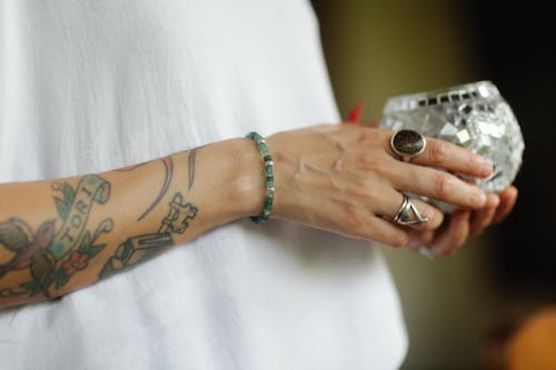 Tattooed Hand with Rings Holding Crystal Glass