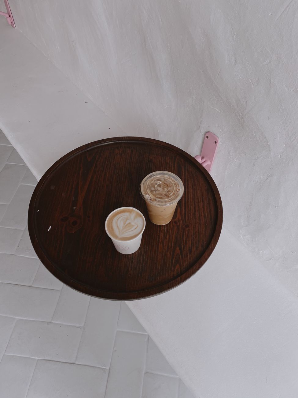 Two disposable coffee cups on a wooden tray against a textured white wall create a minimalist scene.
