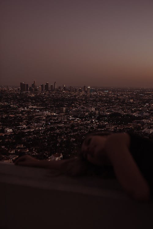 Woman Lying on Wall with City at Night in Background