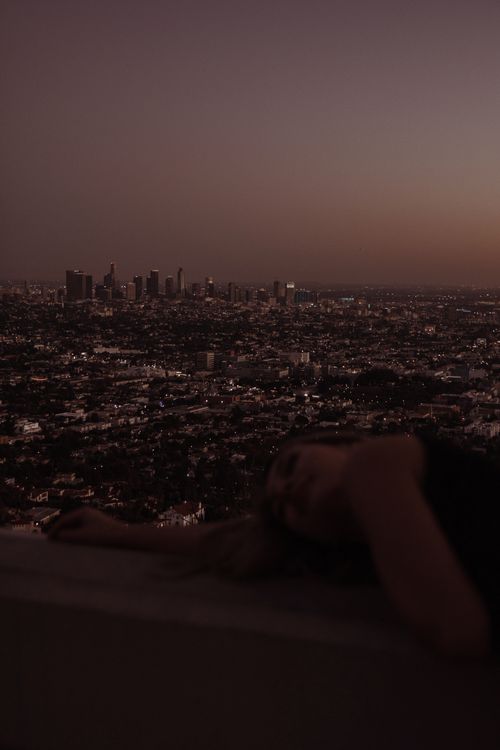 Free A serene scene of a city skyline at dusk with a person lying in the foreground, capturing the essence of a quiet evening. Stock Photo