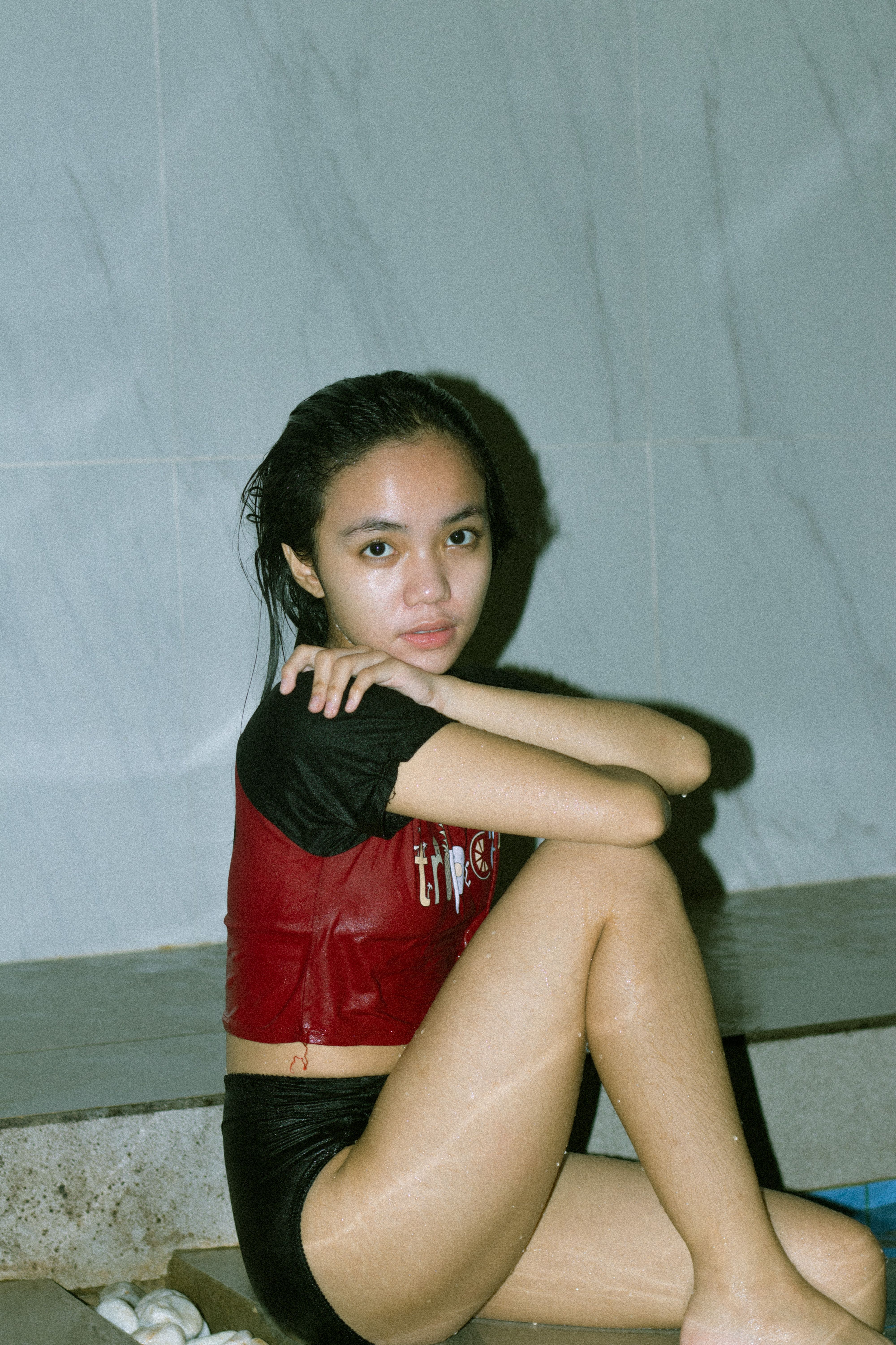 Portrait of an adolescent girl sitting by a pool in swimwear, looking at the camera.