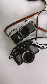 Two classic DSLR cameras displayed on a white surface with camera straps.