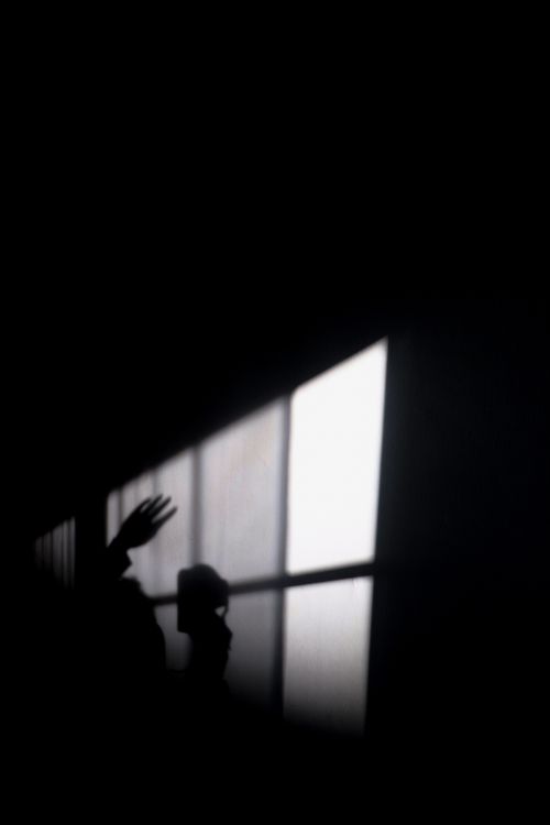 Free A mysterious silhouette with raised hand against a lit window, capturing a sense of intrigue. Stock Photo