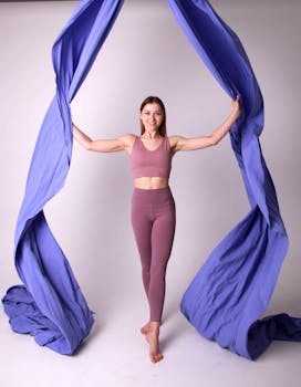 A fit woman in lilac activewear posing with vibrant blue fabric in a studio setting, exuding energy and positivity.