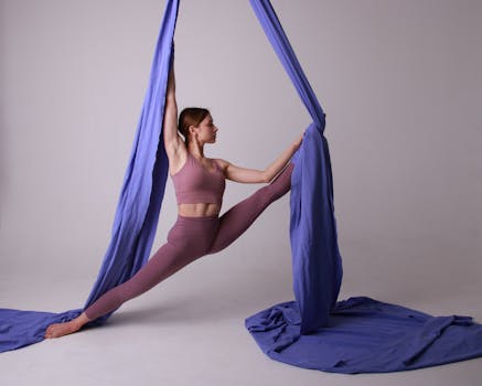 Woman performing a graceful aerial yoga pose using purple silks. Capturing strength and flexibility.