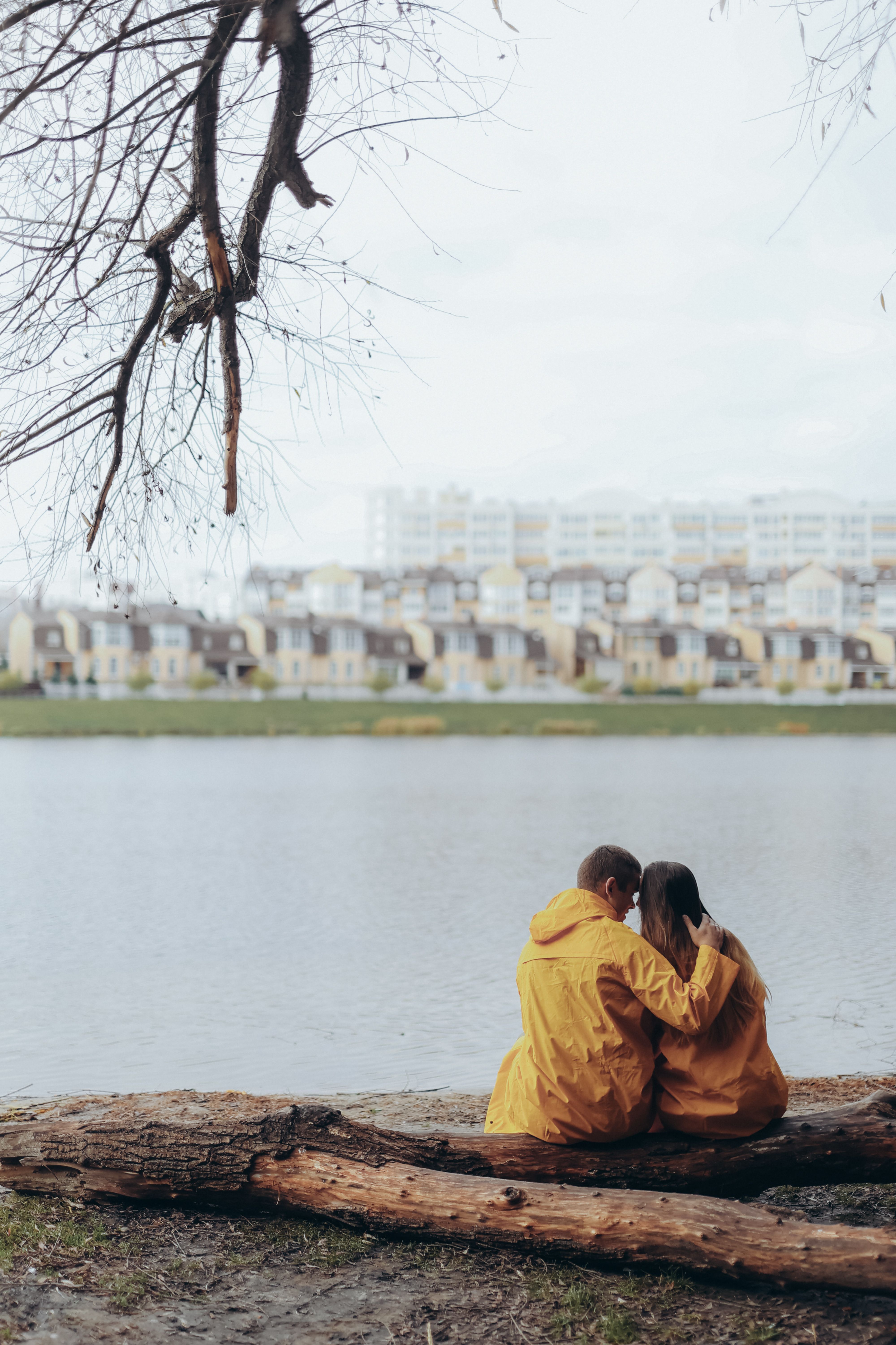 A loving couple in matching jackets embraces by a calm riverside in autumn.