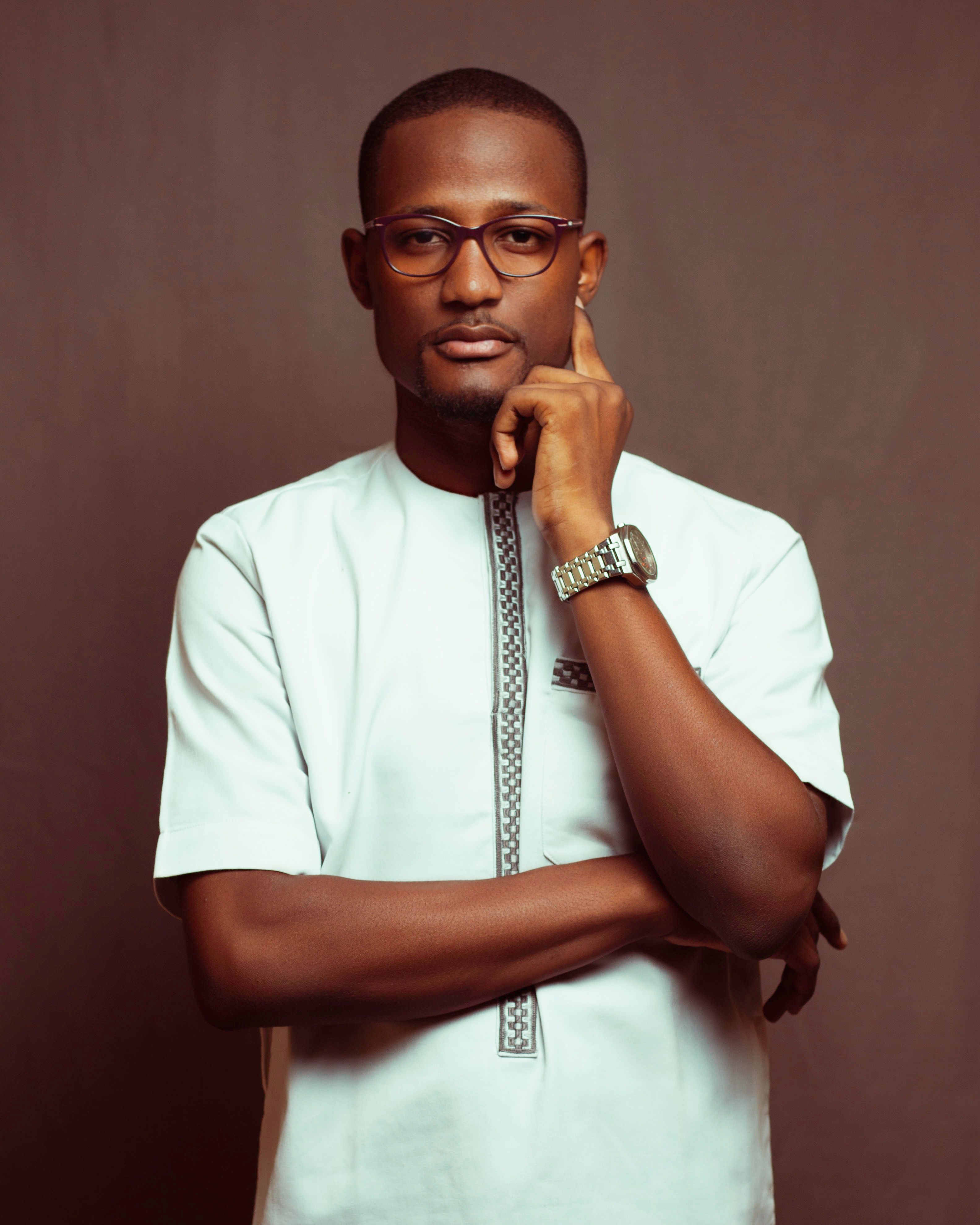 A confident man with eyeglasses poses in a white traditional shirt, showcasing a thoughtful demeanor.