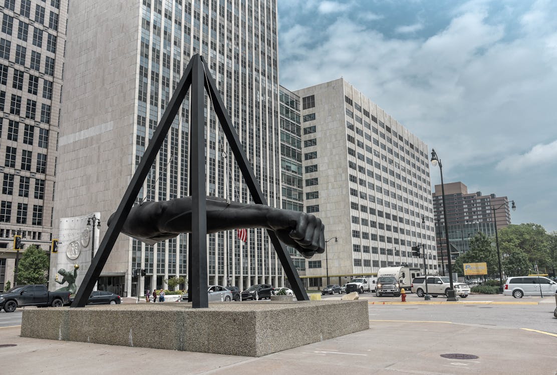 Statue of Human Arm Near Gray Buildings