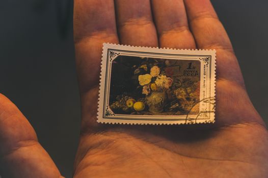 Close-up of a vintage Soviet postage stamp featuring a still life on a person's palm, in warm lighting.