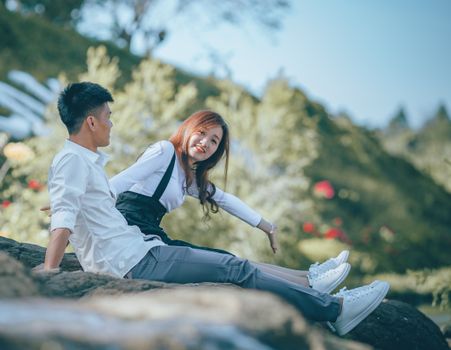 Couple in White Long Sleeve Shirts Sitting on Rock 