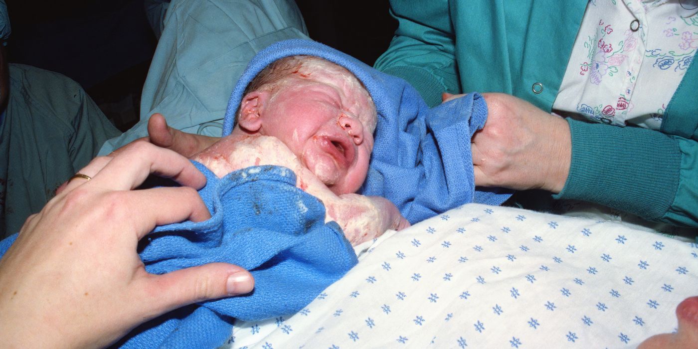 A newborn baby immediately after birth being wrapped in a hospital delivery room.