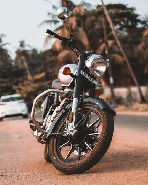 Free Close-up view of a classic motorcycle parked on a tropical road with a blurred background of palm trees. Stock Photo