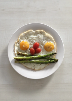 Fun breakfast plate featuring sunny side up eggs, cherry tomatoes, and asparagus arranged as a smiley.