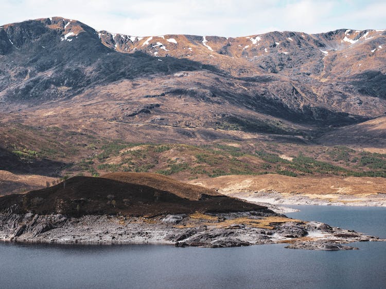 Highlands With Snow Near Body Of Water In Scotland