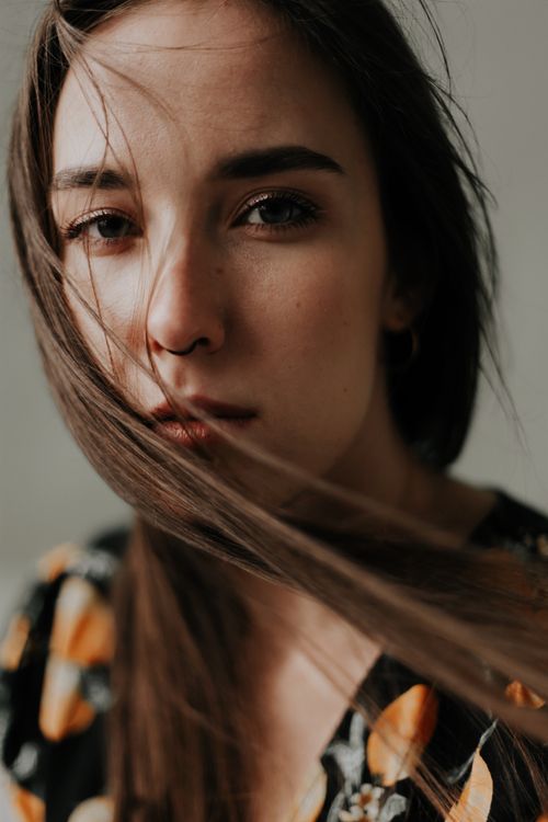 Free Intimate portrait of a woman with wind-swept hair and floral jacket, neutral expression. Stock Photo