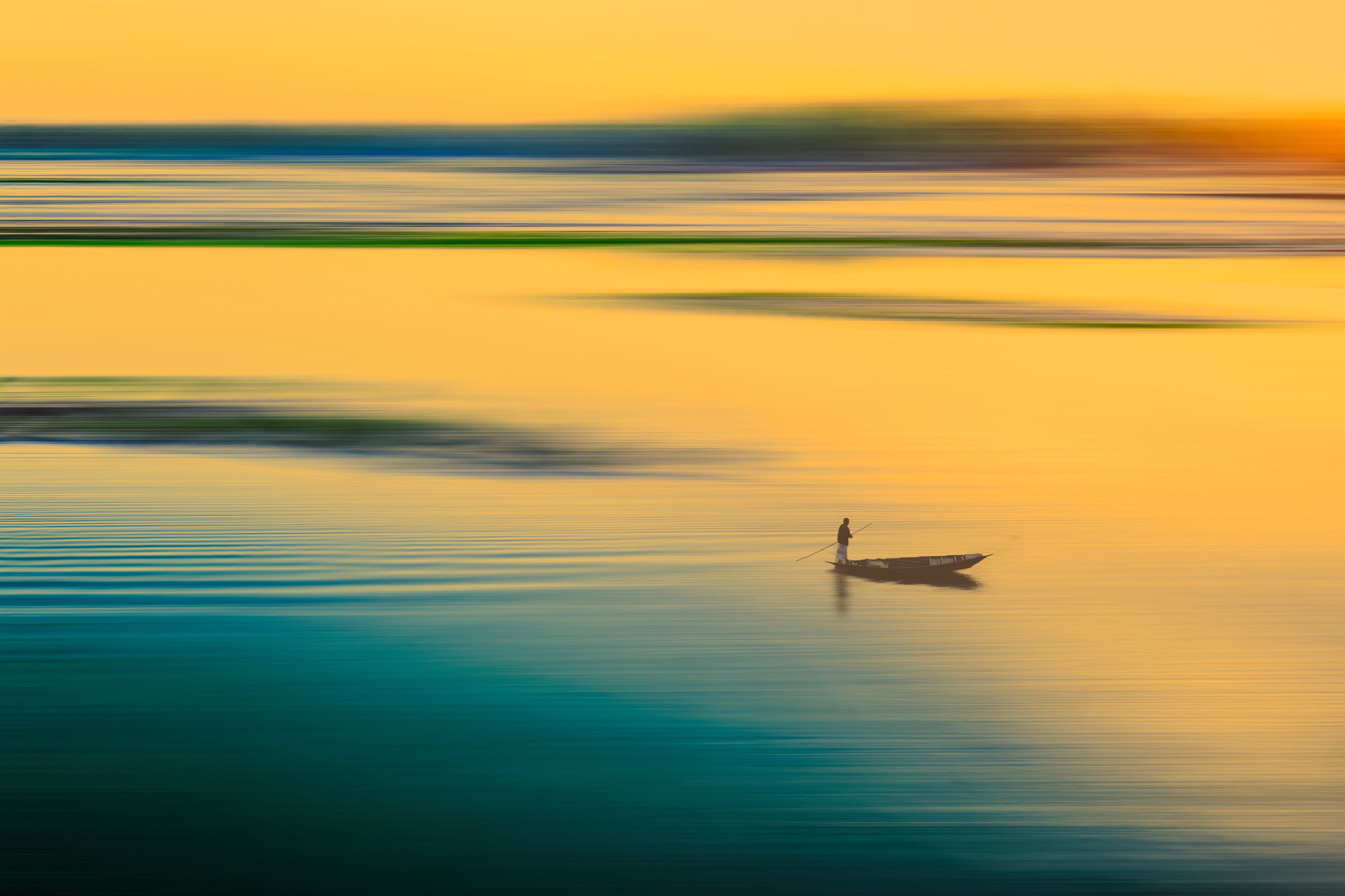 A lone fisherman on a boat amidst tranquil waters during sunset, creating a serene scene.
