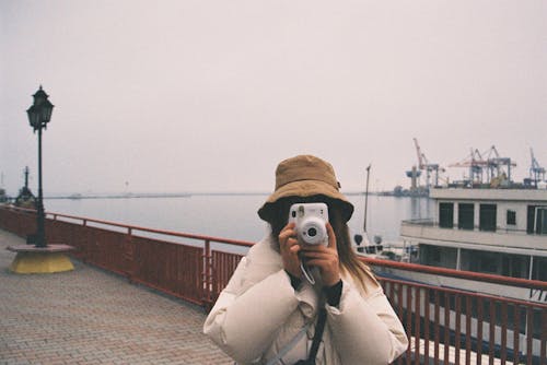 Free Woman in White Coat and Brown Hat Holding Black Camera Stock Photo