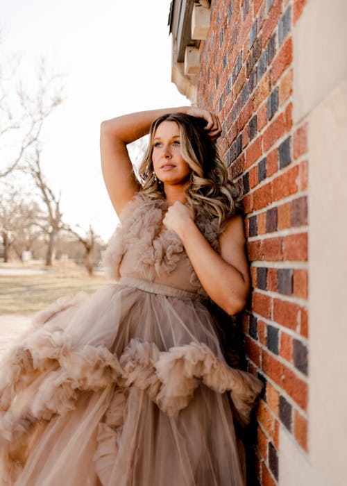 Woman in Brown Dress Leaning on Brick Wall