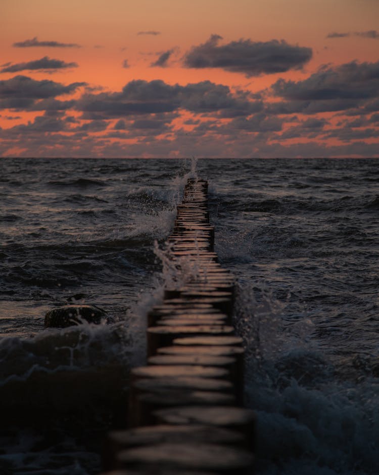 Waves Crashing Over Breakwater At Sunset