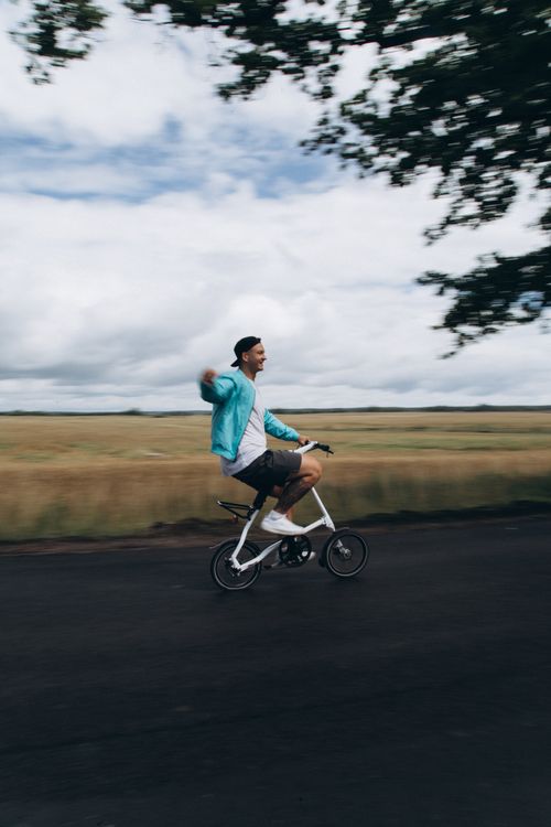 Free A man rides a small bike on a road, surrounded by expansive countryside and white clouds. Stock Photo