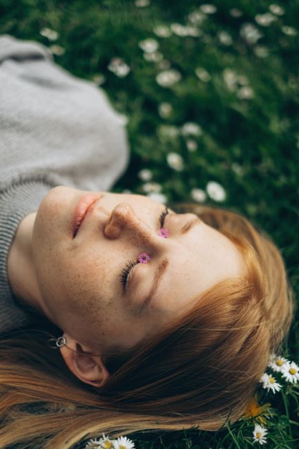 A serene portrait of a woman lying among daisies with eyes closed, capturing tranquility and nature.