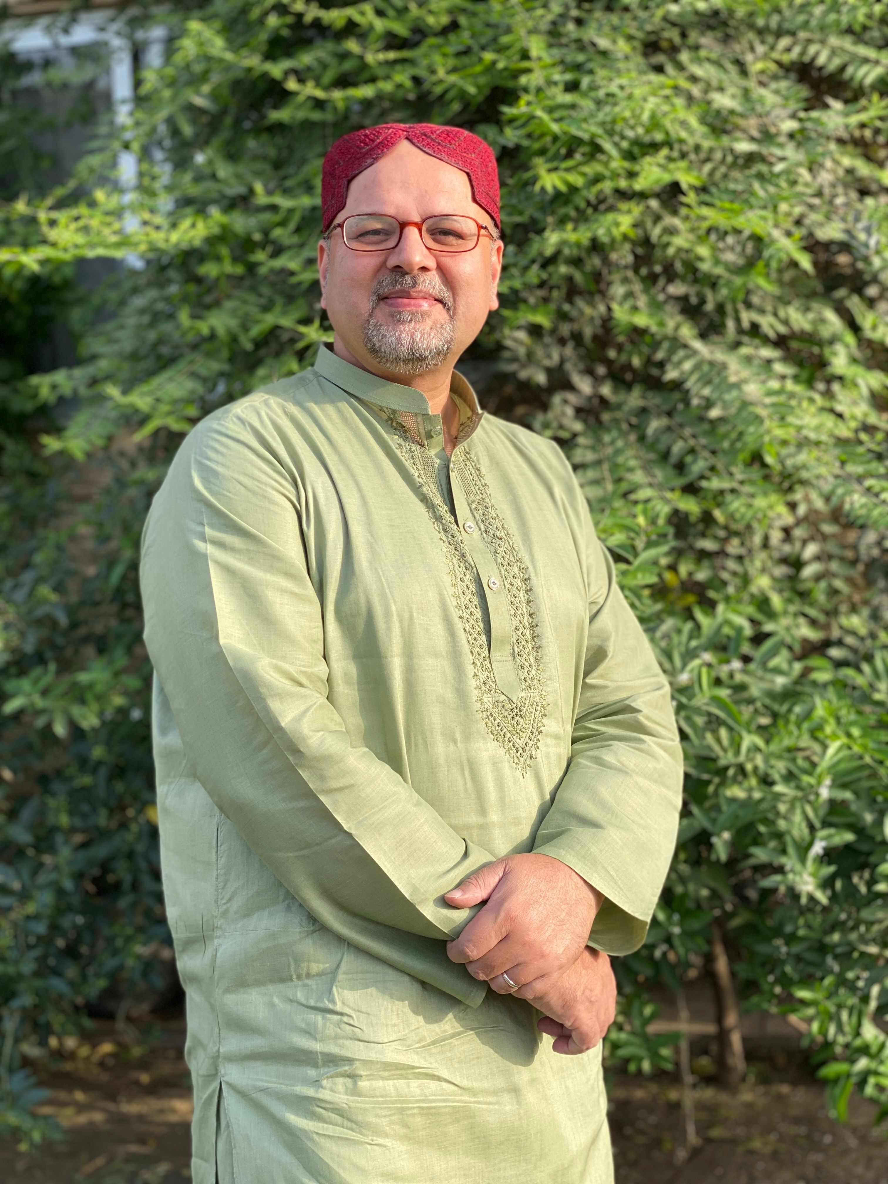 Middle-aged man in traditional kurta standing outdoors, smiling confidently.
