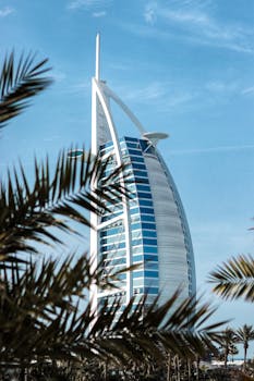 Iconic Burj Al Arab surrounded by palm trees on a clear day in Dubai. Perfect for travel and architecture enthusiasts.