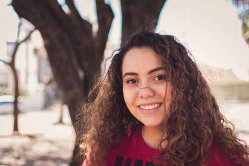 Free Portrait of a smiling young woman with curly hair in a sunny outdoor setting. Stock Photo