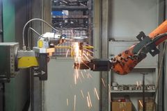 A robotic arm welding in an industrial setting, emitting bright sparks.