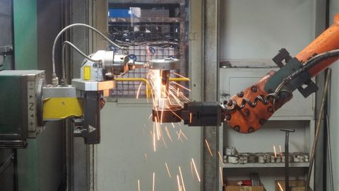 A robotic arm welding in an industrial setting, emitting bright sparks.