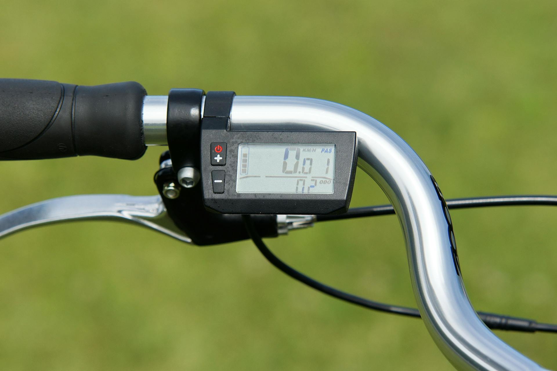 Close-up view of a digital speedometer mounted on bicycle handlebars outdoors.