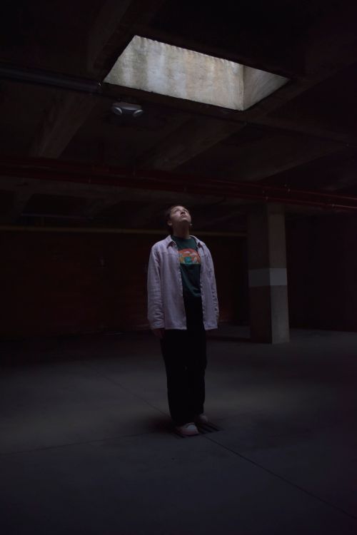 Free A person stands in a dimly lit industrial space, gazing up at a skylight. Stock Photo