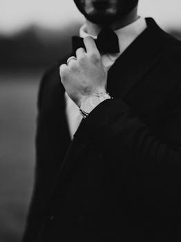 Stylish man in black suit adjusting bow tie, showcasing elegance and sophistication.