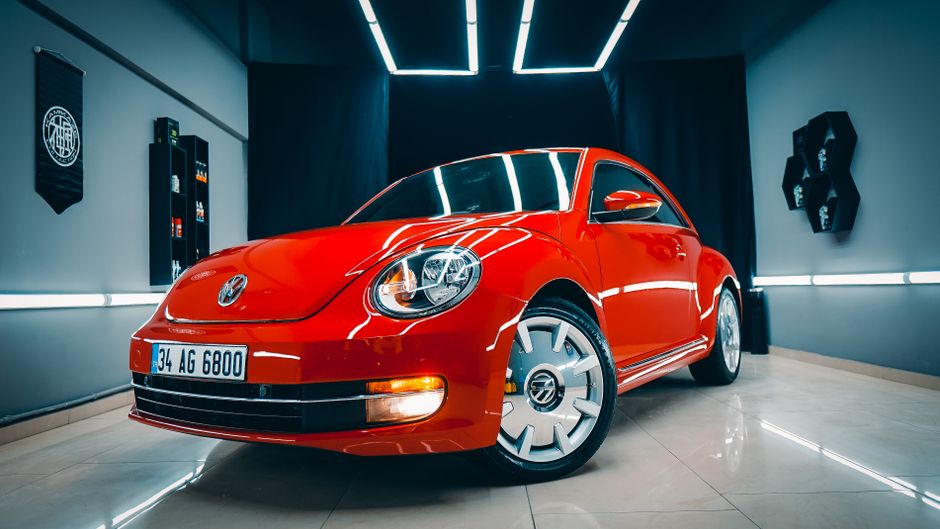 Vibrant red Volkswagen Beetle parked in a sleek indoor showroom, showcasing its classic design.