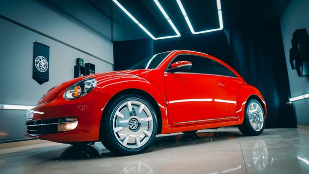 A striking low angle shot of a shiny red Volkswagen Beetle parked indoors on a tiled showroom floor.