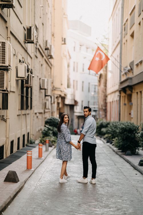 Free A couple holding hands and walking down a quaint street featuring a Turkish flag. Stock Photo
