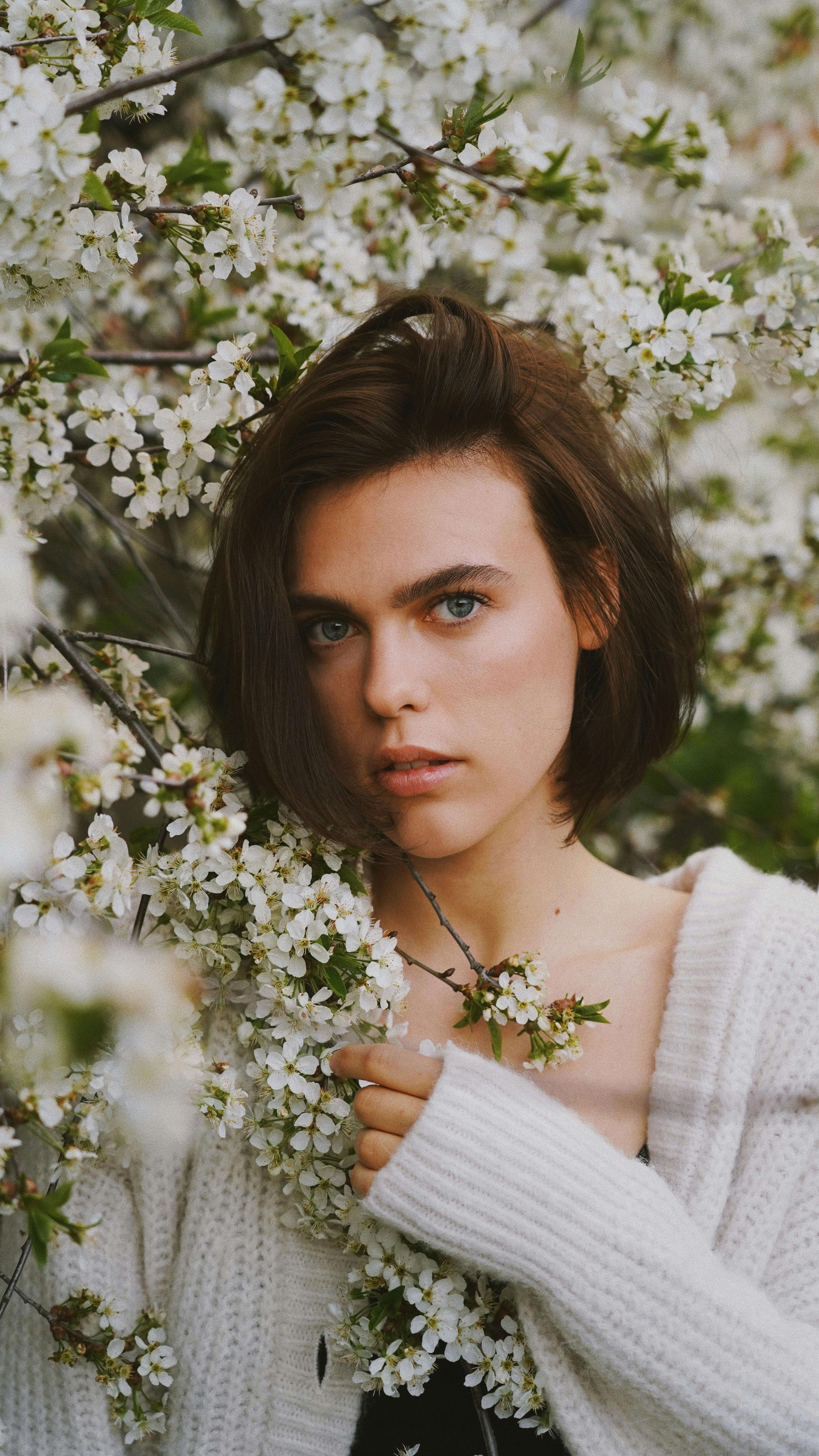 Portrait of a young woman in a white sweater surrounded by spring blossoms.