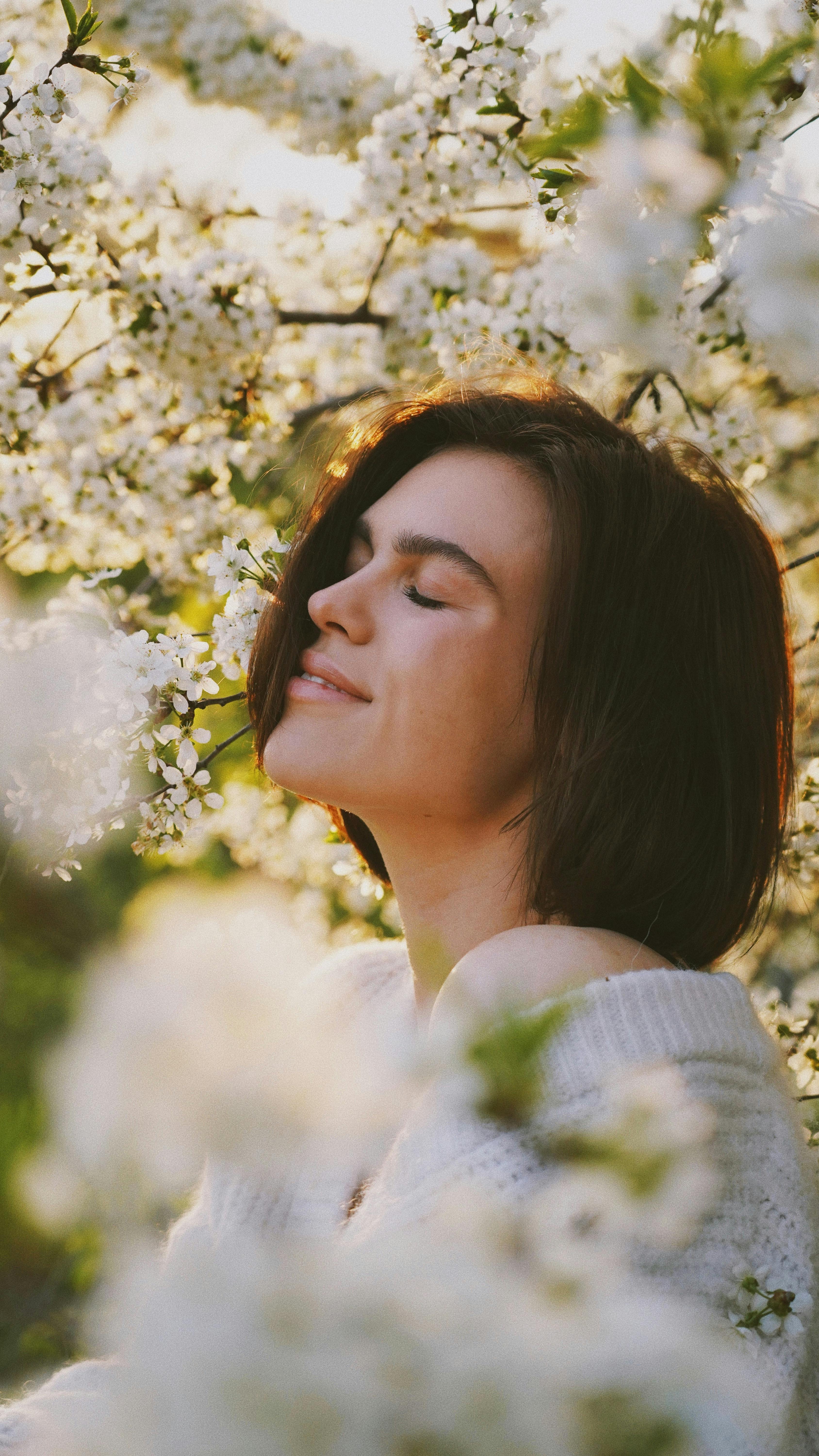 A serene portrait of a woman among blooming spring flowers, eyes closed, feeling the freshness.