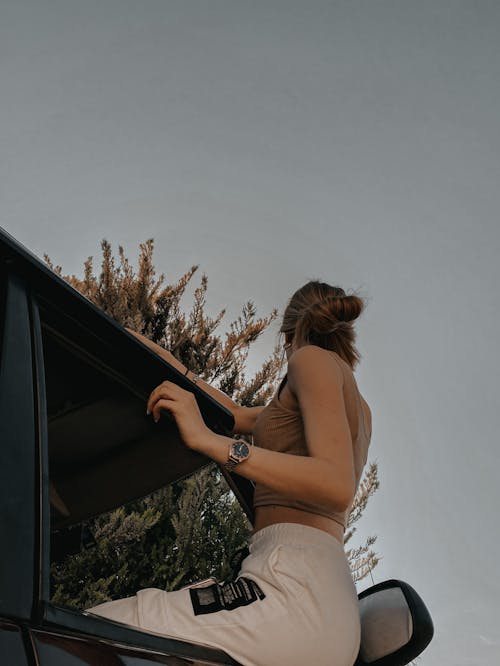 Woman in Brown Crop Top Sitting on the Window of a Moving Car