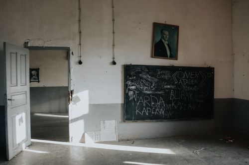 Free An empty, dimly lit classroom with an open door, blackboard, and portrait, evoking a historical atmosphere. Stock Photo