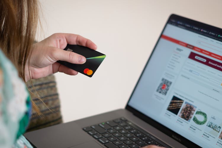 A Person Holding An ATM Card While Typing On Her Laptop